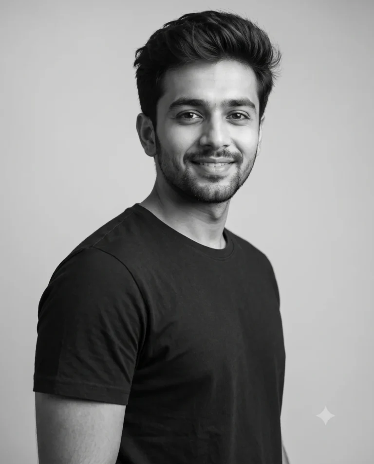 A young man smiling in a black and white studio prompt portrait with soft lighting.