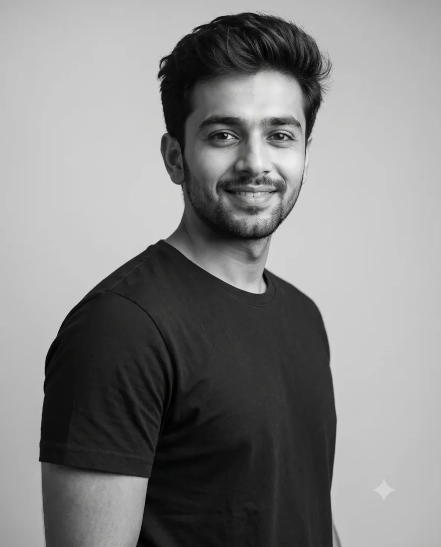 A young man smiling in a black and white studio prompt portrait with soft lighting.